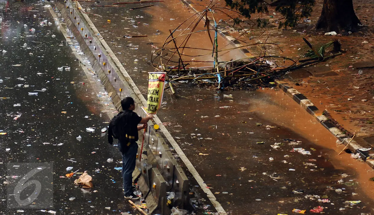 Warga melihat pamplet yang tersisa di jalan Medan Merdeka Barat yang dipenuhi sampah usai perayaan hari Buruh Internasional, Jakarta, Senin (5/1). Ribuan massa buruh ikut dalam perayaan Hari Buruh Internasional 2017. (Liputan6.com/Helmi Fithriansyah)