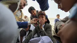 Seorang pria Yaman mengoleskan kosmetik tradisional Kohl ke kelopak mata remaja selama bulan puasa Ramadhan di Masjid Sanaa (16/4/2021).  Di Yaman, salah satu tradisi khas menandai Ramadhan yang masih lestari adalah aksi para pemuda yang merias mata dengan kohl. (AFP/ Mohammed Huwais)