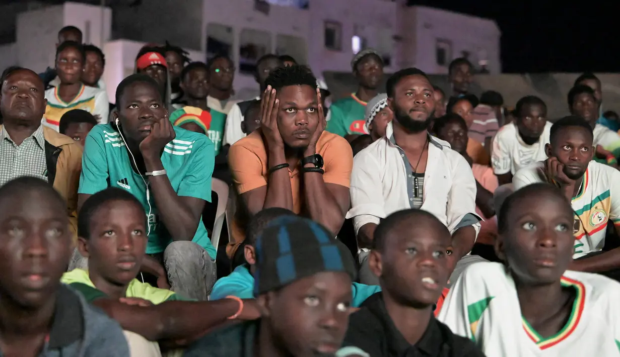 Suporter Senegal bereaksi saat menyaksikan laga babak 16 besar Piala Dunia 2022 saat tim kesayangan mereka melawan Inggris di Qatar, lewat layar video yang dipsang di fan zone di Dakar, Senin (5/12/2022) dini hari WIB. Senegal ditaklukkan Inggris dengan skor 0-3. (Photo by SEYLLOU / AFP)