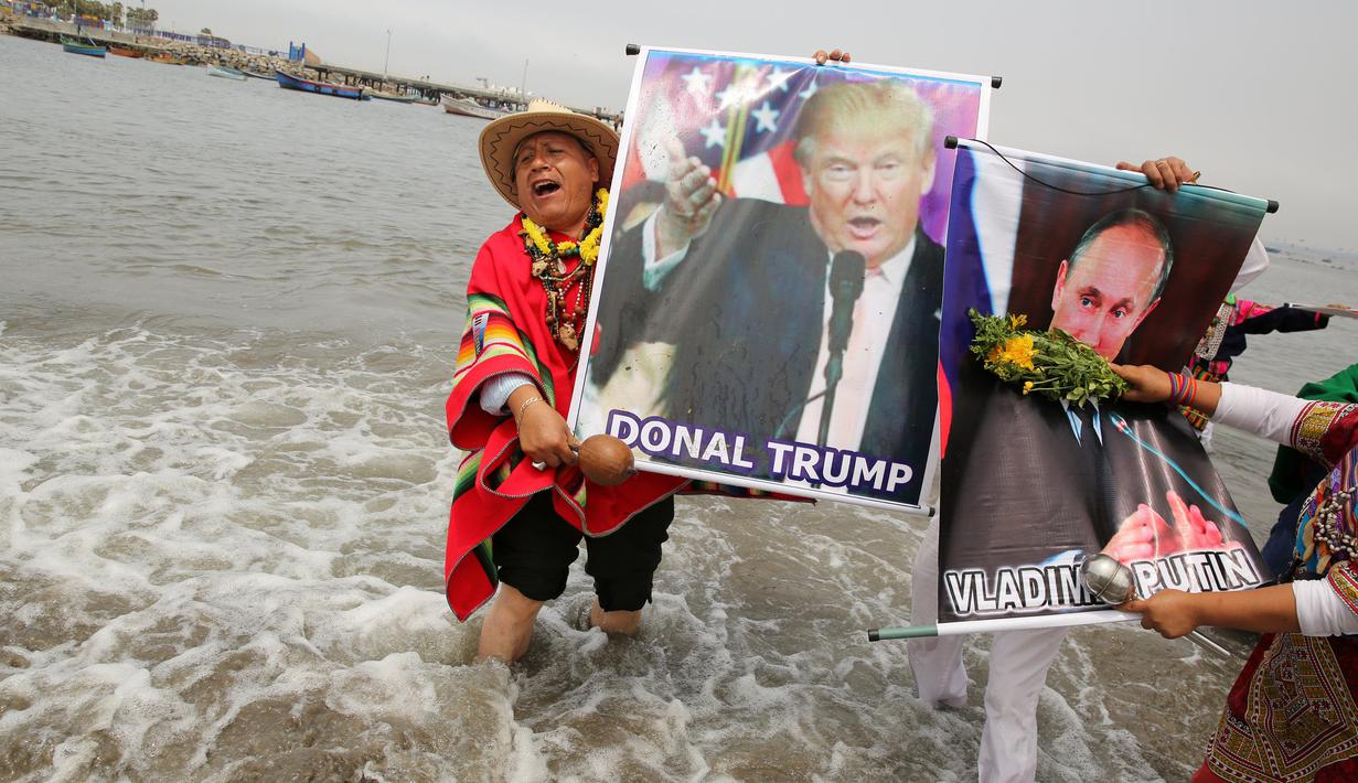 Dukun Peru menunjukkan poster Donald Trump dan Vladimir Putrin saat menggelar ritual di Pantai Agua Dulce di Lima, Peru, (29/12). Pada 2017 dukun Peru memprediksi akan ada keruntuhan ekonomi dunia dan gempa bumi dahsyat. (Reuters/Mariana Bazo)