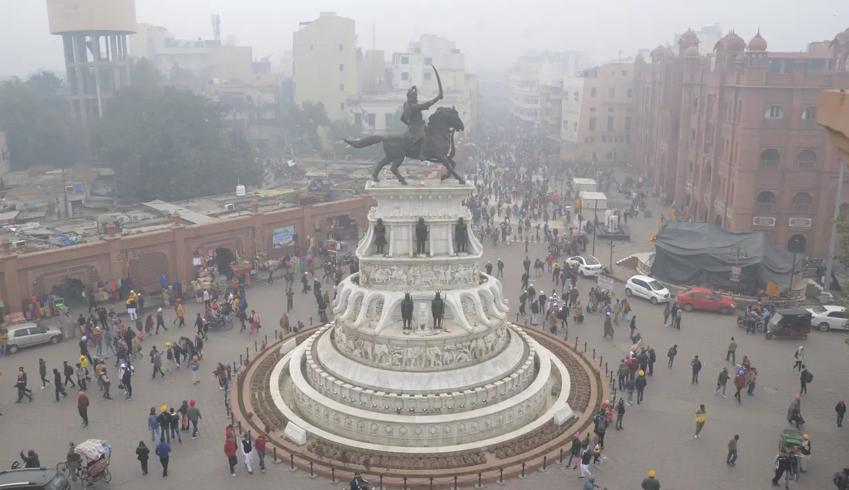 Orang-orang yang berjalan di dekat patung Maharaja Ranjit Singh di tengah kondisi berkabut pada Hari Tahun Baru, di Amritsar (1/1/2021). Kabut tebal mengurangi jarak pandang hingga nol meter, menurut Departemen Meteorologi India (IMD). (AFP/Narinder Nanu)