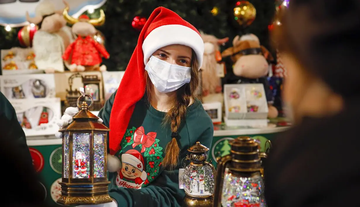 Seorang penjual yang mengenakan masker untuk membantu mengekang penyebaran virus corona COVID-19 menawarkan dekorasi Natal di GUM State Department Store, Moskow, Rusia, Senin (23/11/2020). Dekorasi untuk perayaan Natal dan Tahun Baru sudah menghiasi Rusia.  (AP Photo/Alexander Zemlianichenko)