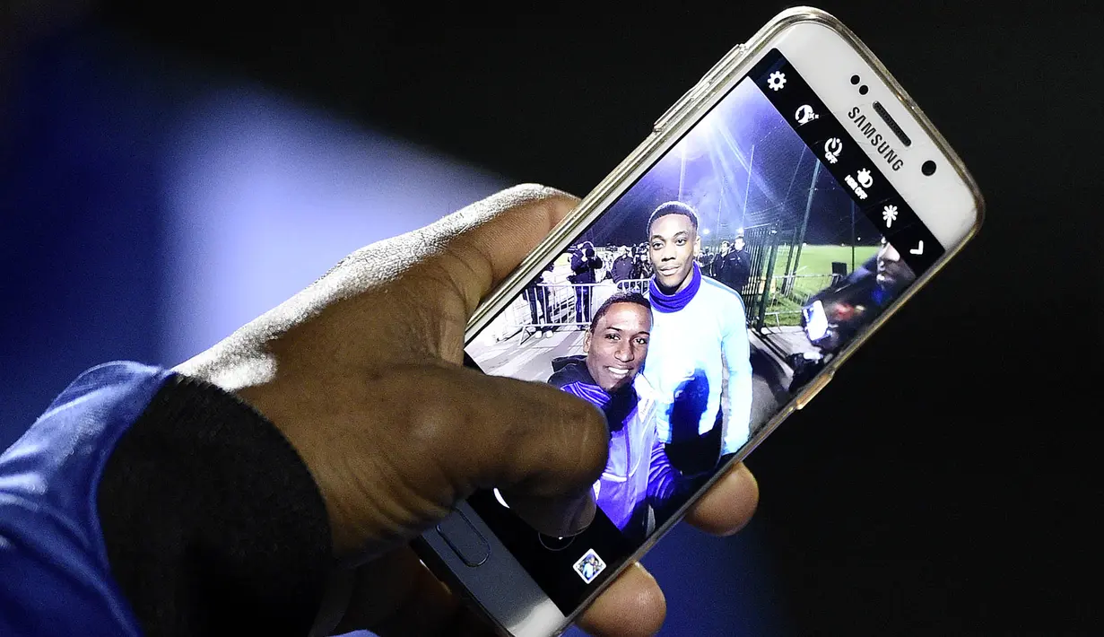 Fans menunjukan foto selfie bersama penyerang MU dan juga timnas Prancis, Anthony Martial usai menonton latihan skuat Les Blues jelang laga persahabatan melawan Jerman di Yvelines, Prancis, Selasa (10/11/2015). (AFP Photo/Franck Fife)