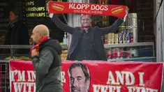 Seorang pedagang Hot Dogs memakai topeng pelatih Liverpool, Jurgen Klopp sambil membentangkan syal saat laga putaran keempat Piala FA antara Liverpool melawan Norwich City di Anfield, Liverpool, Inggris, Minggu (28/01/2024). (AP Photo/Jon Super)