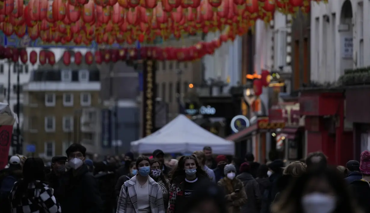 Wanita berjalan melalui Chinatown di Soho di London, Selasa (28/12/2021). Padahal banyak negara Eropa telah memulai pembatasan lebih lanjut pada populasi mereka karena jumlah kasus COVID-19 terkait Omicron meningkat, dan mereka bertujuan untuk menahan penyebaran virus. (AP Photo/Alastair Grant)