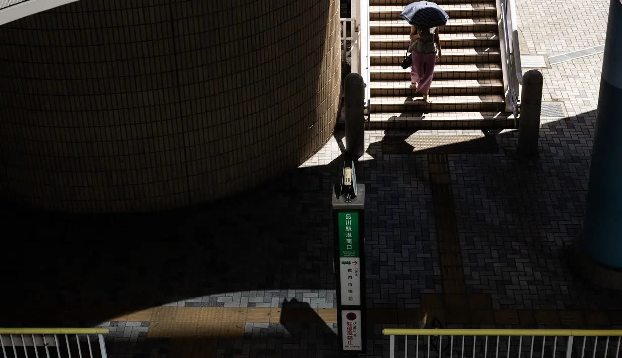 Seorang wanita dengan payung (kanan atas) berjalan menuruni tangga di stasiun kereta api di Tokyo saat keadaan darurat virus corona tetap berlaku di kota itu, Selasa (10/8/2021).  Pemerintah Metropolitan Tokyo mengonfirmasi 2.884 kasus baru covid-19 pada Senin, 9 Agustus 2021. (Yuki IWAMURA / AFP)