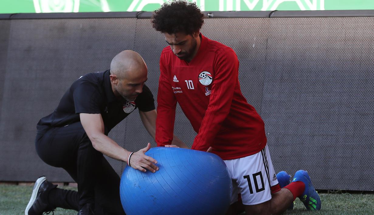 Pemain timnas Mesir Mohamed Salah dibantu tim kesehatan melatih bahunya yang cedera saat pelatihan di stadion Akhmat Arena di Grozny (12/6). Pemain Liverpool ini cedera saat tampil di Final Liga Champions melawan Real Madrid. (AFP Photo/Karim Jaafar)