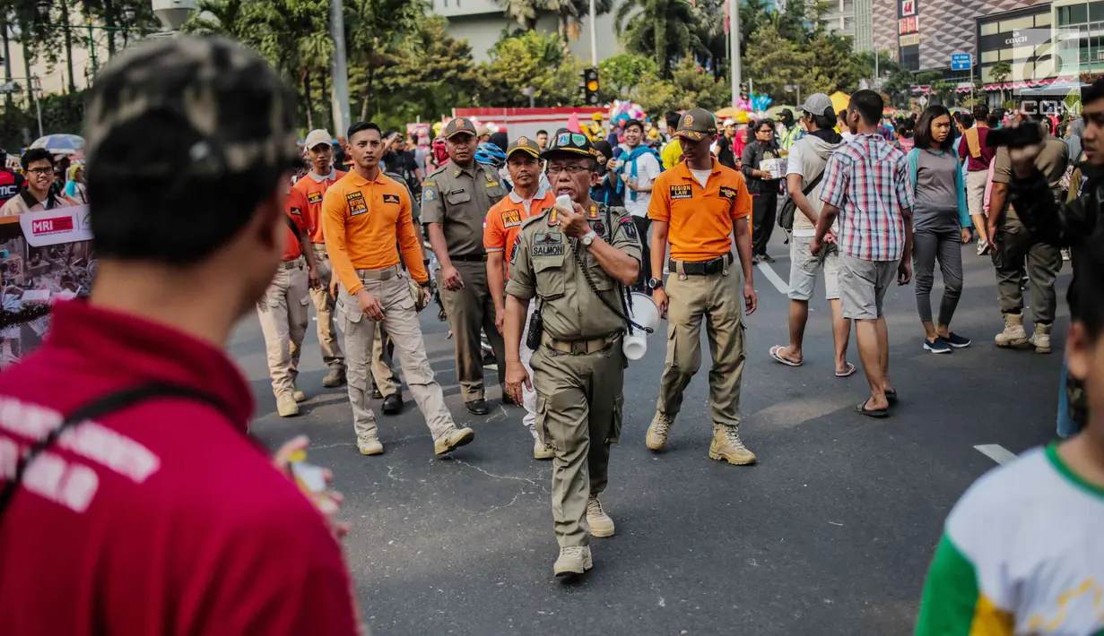 Petugas Satpol PP melakukan sosialisasi saat menertibkan PKL di kawasan car free day (CFD), Bundaran HI, Jakarta, Minggu (4/8/2019). Penertiban dilakukan karena keberadaan PKL membuat tidak nyaman pengunjung CFD yang ingin berolahraga, berorasi, atau sekadar jalan-jalan. (Liputan6.com/Faizal Fanani)