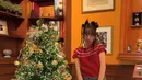 Hyeri berfoto dengan pohon Natal setinggi dirinya yang dihiasi ornamen gold. Ia mengenakan atasan  knit merah lengan pendek dipadukan celana pendek abu-abu senada dengan kaos kakinya. [@hyeri_0609]