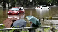 Warga melihat mobil yang terendam banjir di pinggiran barat daya Sydney, Australia, Selasa (8/3/2022). Ribuan warga Sydney diminta untuk mengungsi dari daerah dataran rendah karena hujan lebat dan banjir bandang. (Muhammad FAROOQ/AFP)