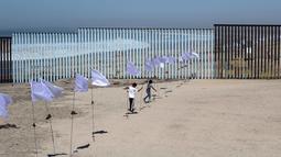 Dua orang anak bermain di seni instalasi kontemporer "Tu huella es el camino, tu bandera es de paz" di Playas de Tijuana, Meksiko (7/10). Karya ini bentuk penghormatan untuk para migran yang melintasi perbatasan Meksiko-AS. (AFP Photo/Guillermo Arias)