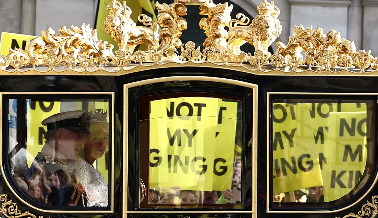 Raja Inggris Charles III dan Ratu Inggris Camilla melakukan perjalanan dengan Diamond Jubilee State Coach melewati para pengunjuk rasa yang memegang plakat "Not My King" dari kelompok anti-monarki Republik saat mereka berdemonstrasi menjelang Pembukaan Parlemen, di seberang Gedung Parlemen di London pada 7 November 2023. (HENRY NICHOLLS/AFP)