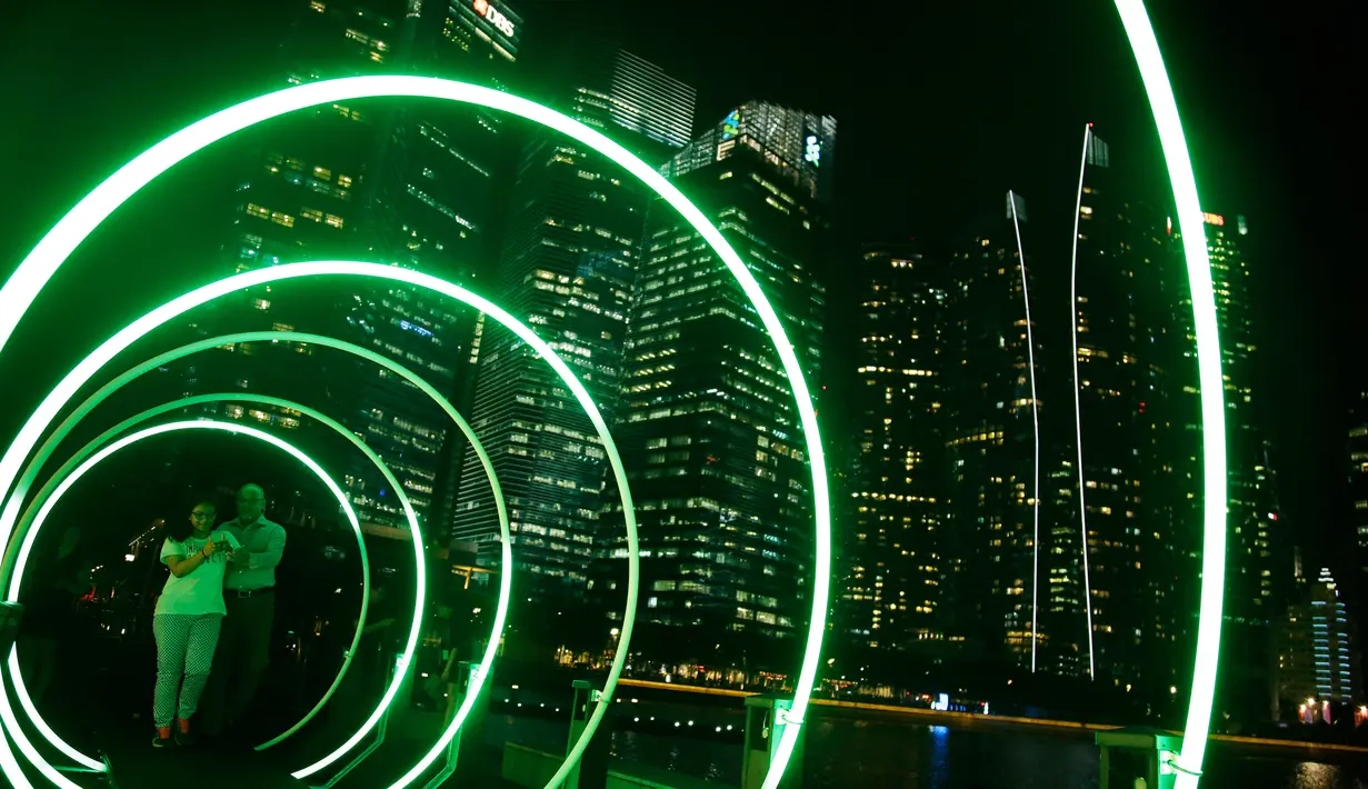 Sepasang pria dan wanita berfoto di lorong jembatan berwarna saat festival Light Marina Bay di Singapura (8/3). Pameran ini menampilkan karya kreatif berskala besar di dalam ruang kota. (AP Photo / Wong Maye-E)