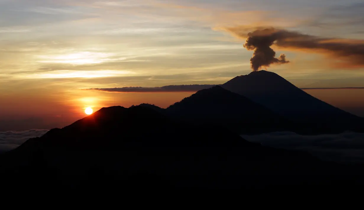 Gunung Agung mengembuskan asap saat matahari terbit (sunrise) terlihat dari Kintamani, Bali, Rabu (13/12). Visual Gunung Agung tampak cerah, asap yang keluar dari kawah gunung itu masih rutin keluar meski tidak secara menerus. (AP Photo/Firdia Lisnawati)