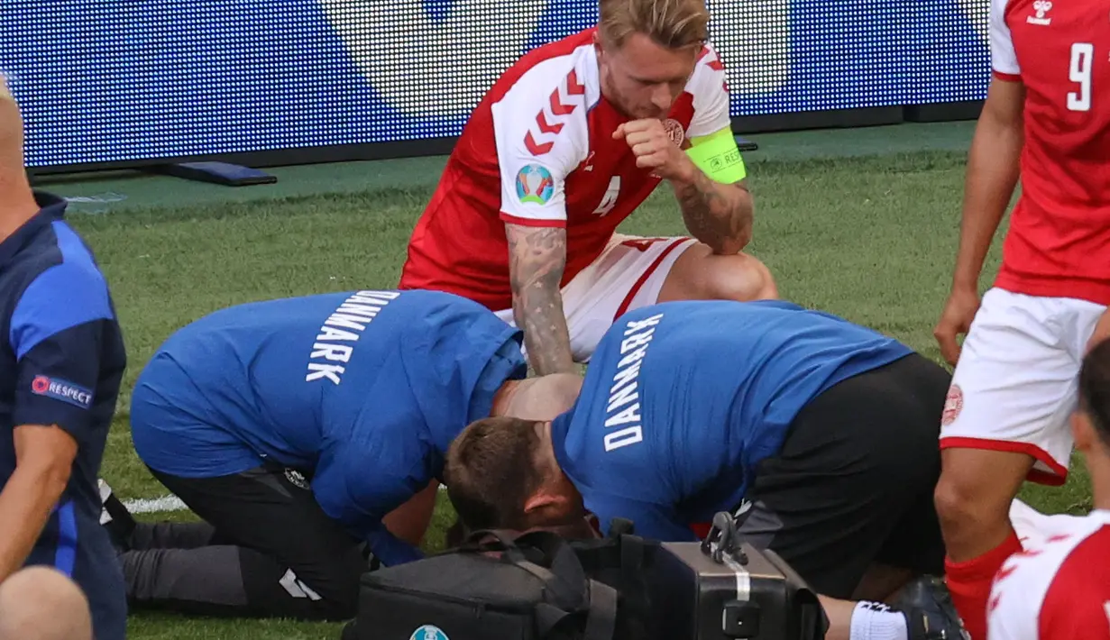 Bek timnas Denmark, Simon Kjaer (belakang) mengamati saat paramedis merawat rekan setimnya Christian Eriksen (tidak terlihat) yang pingsan di lapangan pada laga Denmark vs Finlandia di Grup B Euro 2020 di Parken Stadium, Copenhagen, Sabtu (12/6/2021). (WOLFGANG RATTAY / POOL / AFP)