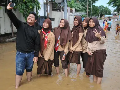 Sejumlah pelajar berfoto di jalanan kawasan Kelurahan Bukit Duri, Tebet, Jakarta yang terendam banjir, Selasa (8/3/2016). Banjir tersebut akibat meluapnya Sungai Ciliwung. (Liputan6.com/Gempur M Surya)