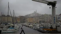 Seorang wanita berjalan di tengah hujan di Pelabuhan Vieux saat badai di Marseille, Prancis selatan, Senin (4/10/2021). Wilayah Prancis selatan dalam siaga untuk hujan lebat dan banjir. (AP Photo/Daniel Cole)