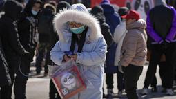 Seorang wanita membawa boneka maskot Olimpiade Bing Dwen Dwen melewati ratusan warga yang berbaris di luar toko yang menjual memorabilia resmi Olimpiade di Beijing, 21 Februari 2022. Boneka maskot Olimpiade masih tetap populer meskipun Olimpiade Musim Dingin telah berakhir. (AP Photo/Andy Wong)