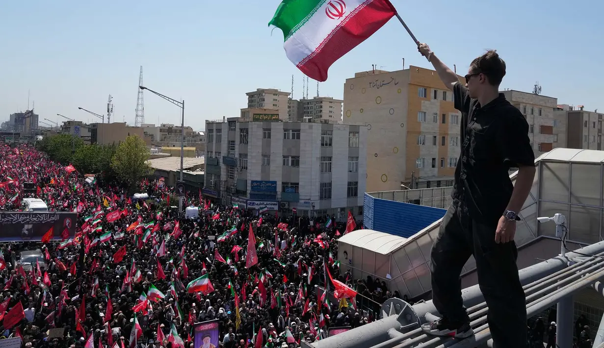 Seorang pria memegang bendera Iran saat truk yang membawa peti jenazah Pemimpin Tertinggi Iran Ayatollah Ali Khamenei dan anggota keluarganya yang terbunuh melintas  di Teheran, Iran, Senin, 6 Juli 2026. (AP Photo/Vahid Salemi)