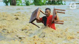 Warga membawa barang miliknya saat banjir bandang  di Kabupaten Bone Bolango, Gorontalo (11/6/2020). Data sementara yang diterima dari BPBD Kabupaten Bone Bolango sekitar 1.078 kepala keluarga serta 5.407 jiwa terdampak banjir bandang. (Liputan.com/Arfandi Ibrahim)