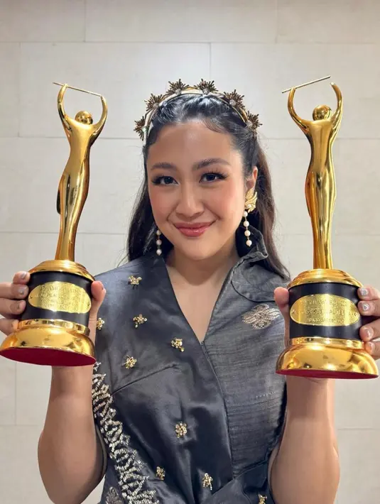 Sherina Munaf berhasil meraih dua piala sekaligus. Di momen itu, ia tampil vest selempang hitam dengan detail bordir emas karya TANGAN Privé, yang dipadukan dengan rok tenun berwarna merah. Penampilannya tampak elegan dan khas dengan sentuhan budaya Indonesia. [@sherinamunaf].