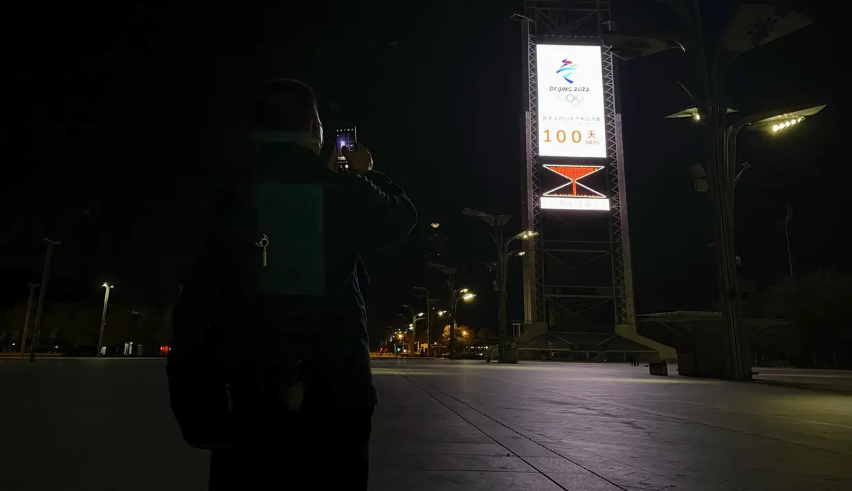 Seorang pria mengambil foto jam hitung mundur yang menunjukkan 100 hari menuju pembukaan Olimpiade Musim Dingin Beijing 2022, di Olympic Park di Beijing, Selasa (26/10/2021). Olimpiade Musim Dingin Beijing 2022 akan berlangsung 4 hingga 20 Februari. (LEO RAMIREZ / AFP)