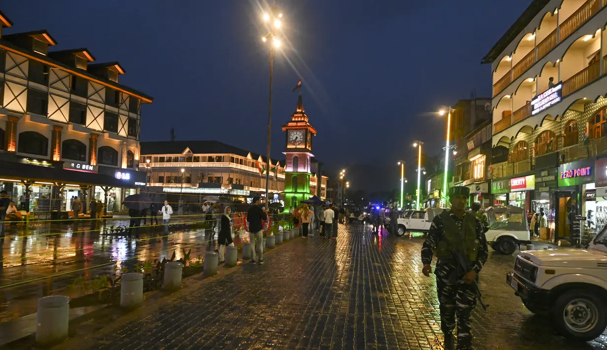 Seorang tentara paramiliter India berjaga di dekat menara jam yang diterangi bendera nasional India pada malam Hari Kemerdekaan negara itu di Srinagar pada 14 Agustus 2023. (Photo by Tauseef MUSTAFA / AFP)