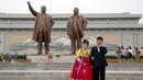 Pasangan pengantin berdiri di dekat patung perunggu raksasa pemimpin Korea Utara Kim Il Sung dan Kim Jong Il dalam peringatan berakhirnya Perang Dunia II dan pembebasan dari kolonial Jepang di Pyongyang, Korut, Rabu (15/8). (AP Photo/Ng Han Guan)