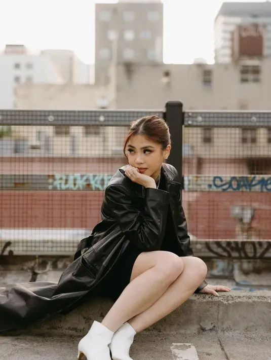 Pesona Clarissa mengenakan outfit serba hitam. Ia memadukan sebuah dress hitam dengan trench coat dari kulit yang juga berwarna hitam, dan midi boots putih. [Foto: Instagram/clarissatanoe]