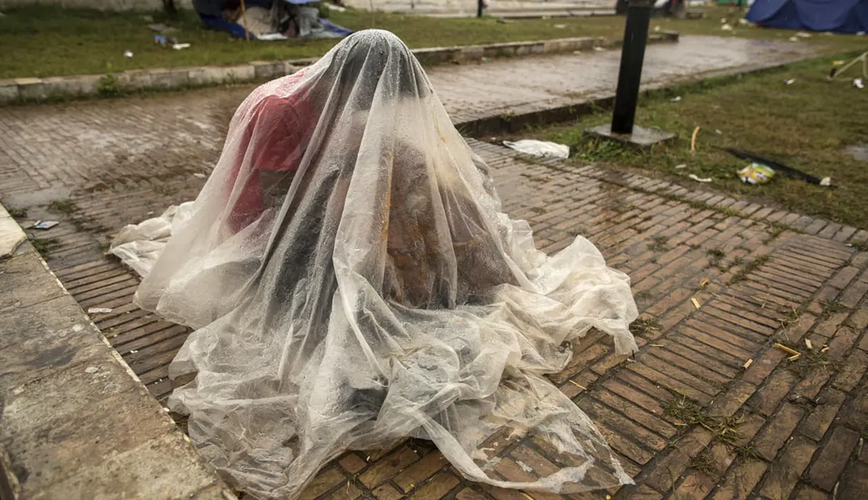 Pengunjuk rasa anti-pemerintah Pakistan berlindung di bawah lembaran plastik saat hujan deras menuntut pengunduran diri Perdana Menteri Nawaz Sharif di Islamabad, (4/9/2014). (REUTERS/Zohra Bensemra)