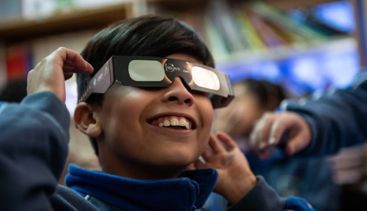 Seorang anak sekolah mencoba kaca mata khusus untuk melihat gerhana matahari total di sekolah Pedro Pablo Munoz di La Higuera, Wilayah Coquimbo, di gurun Atacama, Santiago, Chile (1/7/2019). AFP Photo/Martin Bernetti)