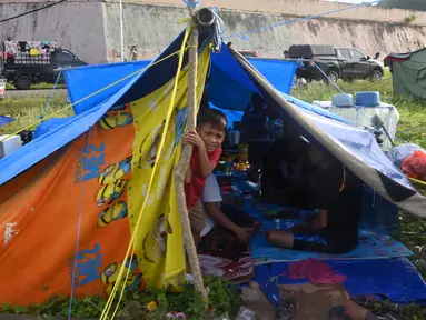 Seorang anak laki-laki mengintip dari tenda ketika orang-orang yang terkena gempa tinggal di kamp sementara setelah gempa berkekuatan 6,2 di Mamuju, Senin (18/1/2021). Ratusan jiwa telah mengungsi di sejumlah posko pengungsian karena rumah mereka rusak akibat gempa. (AFP/Adek Berry)