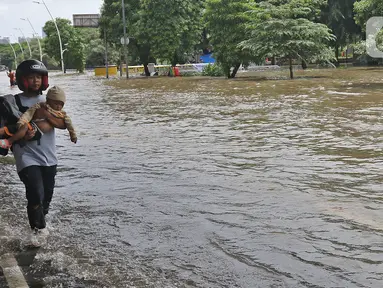 Warga melintasi banjir di Jalan Ahmad Yani, Cempaka Putih, Jakarta, Minggu (23/2/2020). Banjir yang terjadi dari dini hari tadi melumpuhkan akses jalan tersebut. (Liputan6.com/Herman Zakharia)