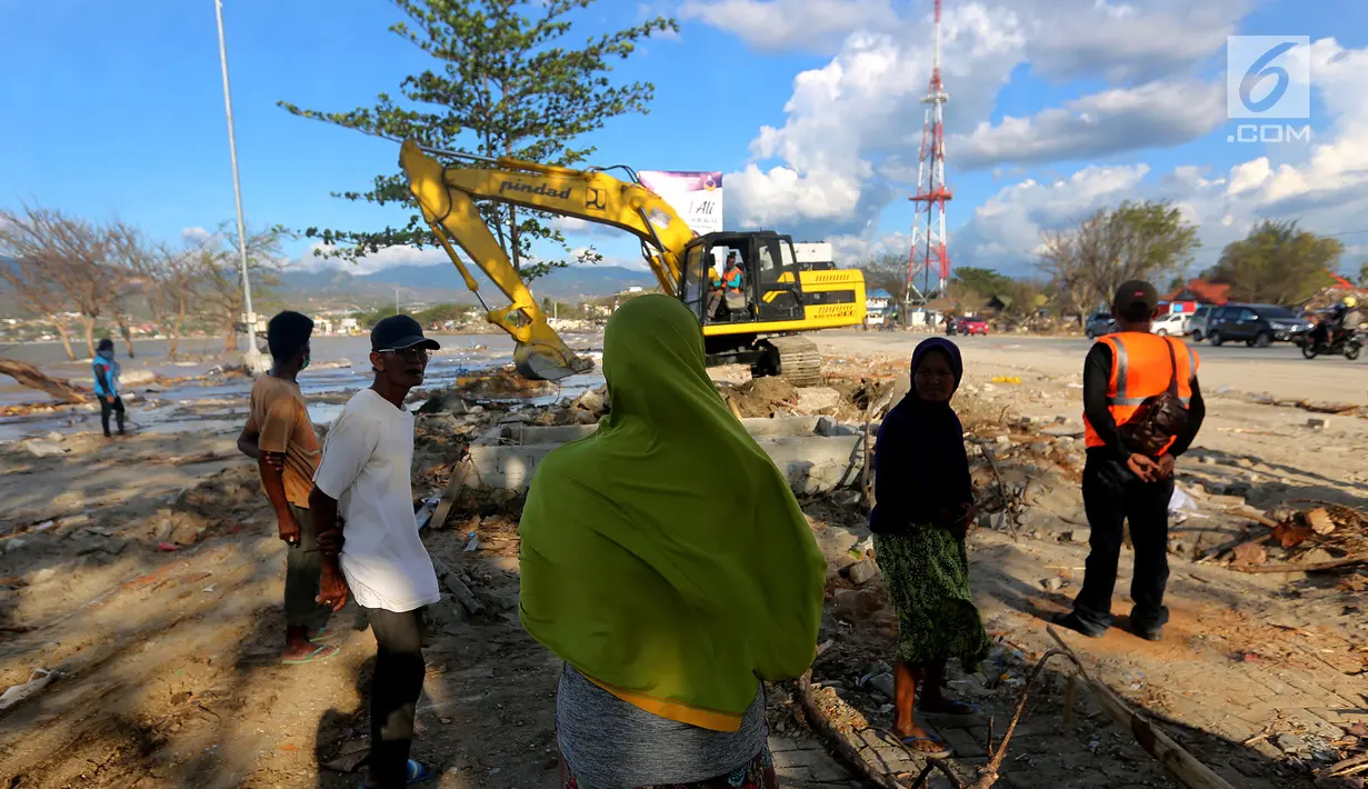 Seorang ibu bernama Lita menyaksikkan proses evakuasi anaknya, Nanang Kosim (20) menggunakan alat berat yang diduga masih tertimbun di dalam tanah pascagempa dan tsunami Palu di Pantai Talise, Sulawesi Tengah, Senin (8/10). (Liputan6.com/Fery Pradolo)