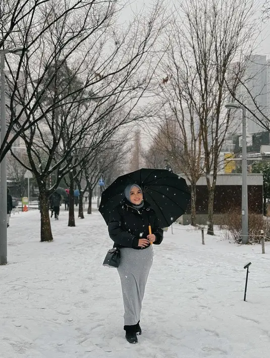Saat menikmati salju, Aurel tampil cantik dengan outer hitam dan rok abu. Dia terlihat memakai payung agar tidak terkena salju secara langsung
