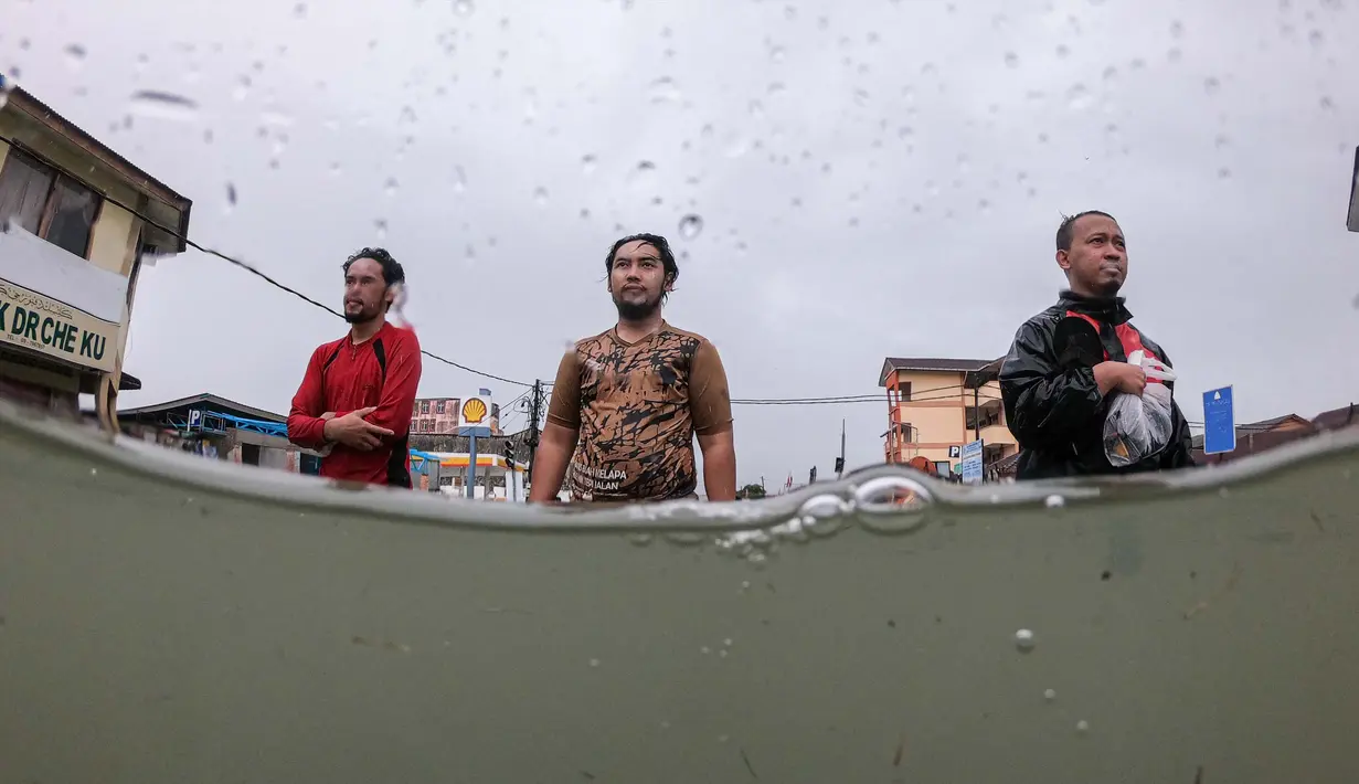 Orang-orang menyeberangi jalan yang tergenang air saat hujan deras di Pasir Puteh, di negara bagian Kelantan, Malaysia, pada tanggal 30 November 2024. (MOHD RASFAN/AFP)
