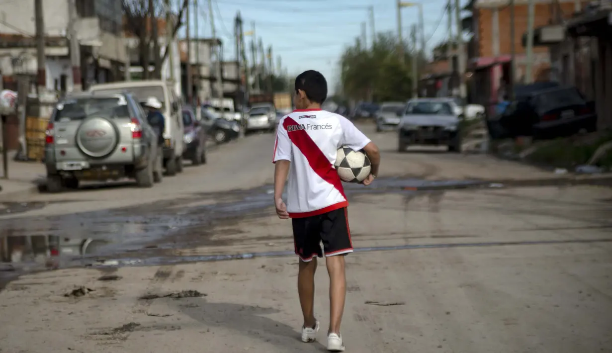 Daniel Dorado dari Argentina mengenakan jersey River Plate berjalan pulang ke rumahnya di daerah kumuh Costa Eperanza, Buenos Aires, 12 September 2020. Daniel, 12, yang bersekolah di sekolah sepak bola Angel Labruna bermimpi menjadi pemain divisi pertama di klub River Plate. (ARIEL TIMY TORRES/AFP)