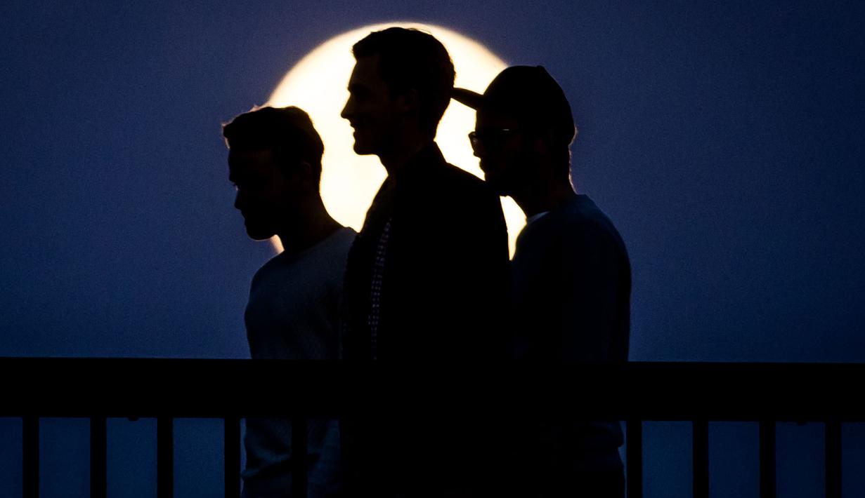 Tiga pria berjalan melintasi jembatan Ignatz Bubis saat tampak bulan purnama di Frankfurt am Main, Jerman barat,(10/5). (AFP Photo/dpa/Frank Rumpenhorst/Germany Out)