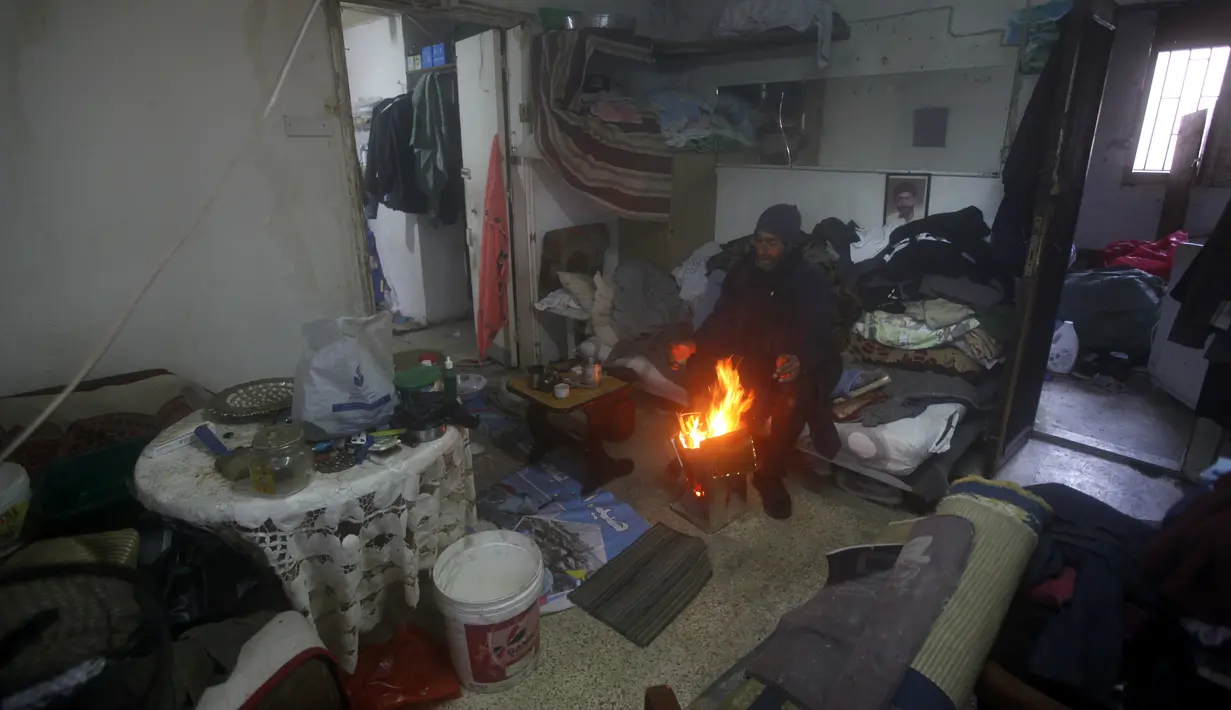 Seorang pria menghangatkan diri di sekitar api unggun di dalam kamar atapnya, di kota pelabuhan selatan Sidon, Lebanon, 19 Januari 2022. Badai salju di Timur Tengah telah membuat banyak warga Lebanon dan Suriah berebut mencari cara untuk bertahan hidup. (AP Photo/Mohammed Zaatari)
