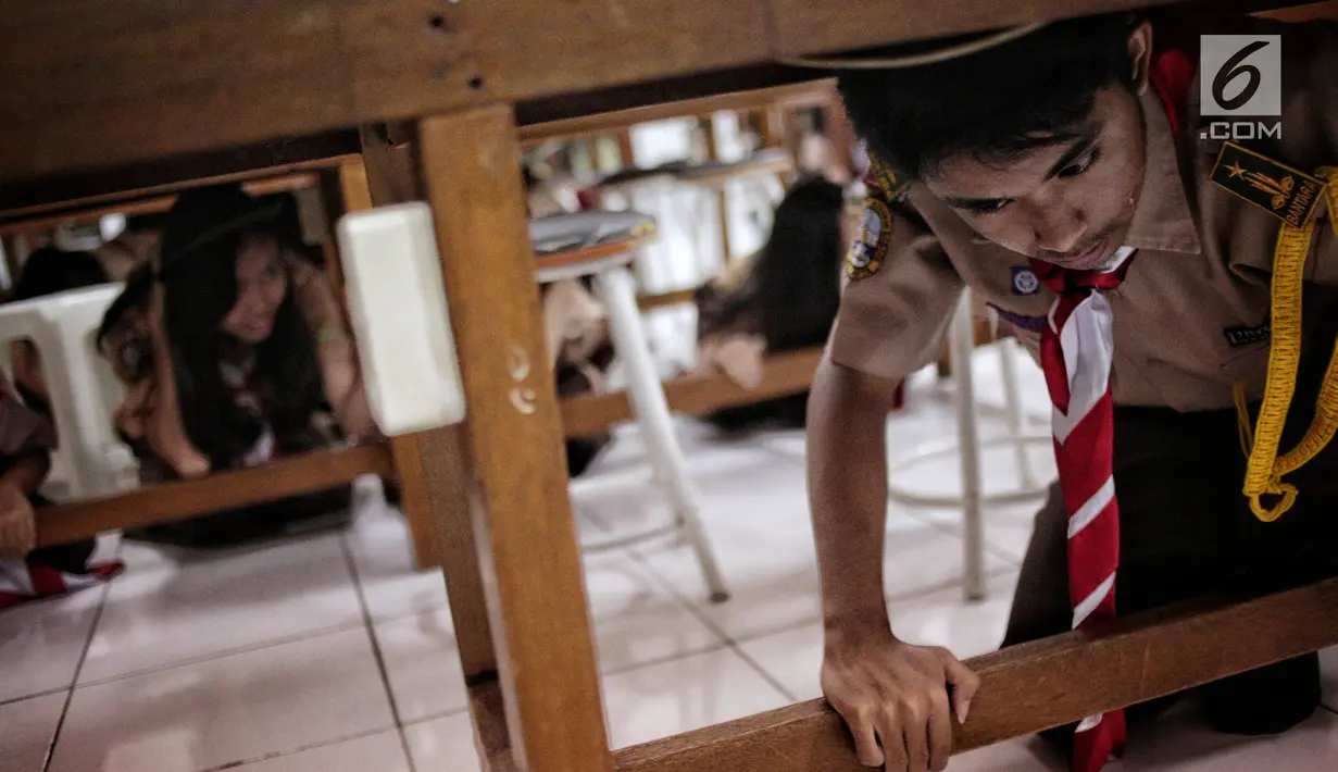 Sejumlah siswa berlindung di bawah meja saat simulasi bencana di SMA Negeri 78 Jakarta, Rabu (23/1). Kegiatan itu untuk pengenalan kepada siswa-siswi dengan program siaga bencana berupa simulasi evakuasi gempa dan tsunami. (Liputan6.com/Faizal Fanani)