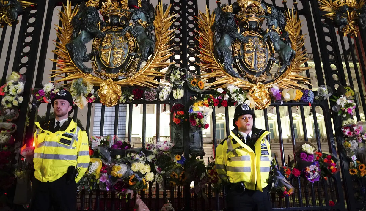 Petugas polisi berdiri di antara karangan bunga yang ditinggalkan di luar Istana Buckingham setelah pengumuman meninggalnya Ratu Elizabeth II, di London, Kamis, 8 September 2022. (Victoria Jones/PA via AP)