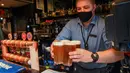 Seorang bartender menyajikan bir di sebuah pub di Melbourne, Australia, Jumat (22/10/2021). Saat ini, 70 persen warga Melbourne sudah divaksin sehingga kebijakan lockdown mulai bisa dilonggarkan. (William WEST/AFP)
