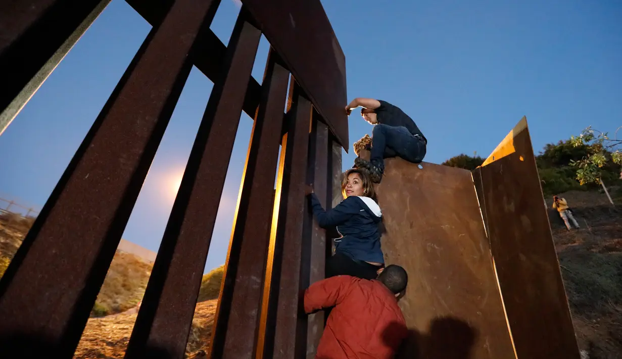 Sejumlah imigran Amerika Tengah memanjat pagar perbatasan ke sisi AS, dari Playas de Tijuana, Meksiko (3/12). Ribuan imigran dari Amerika Tengah melakukan perjalanan menuju Amerika Serikat dalam rombongan atau karavan. (AP Photo/Rebecca Blackwell)
