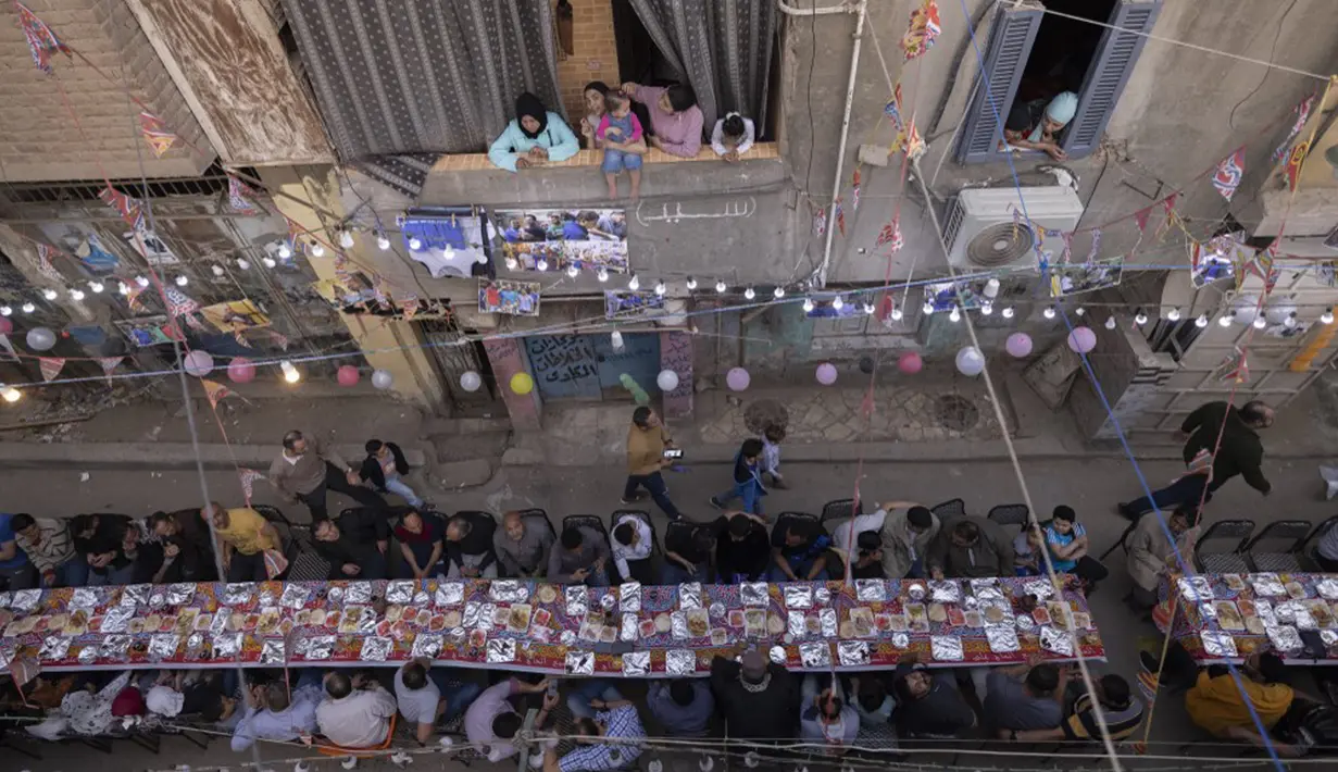 Umat muslim berkumpul di meja sepanjang jalan untuk berbuka puasa bersama dalam jamuan buka puasa massal pada hari ke-15 bulan suci Ramadhan di pinggiran Matariya, timur laut Kairo, Mesir, 16 April 2022. (Khaled DESOUKI/AFP)