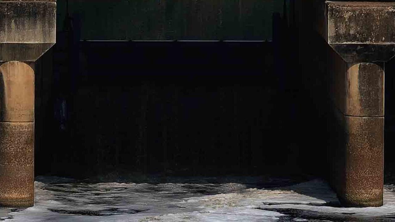 Pengguna sepeda melintas di atas jembatan pintu air Malaka Sari saat busa putih yang berasal dari limbah deterjen mengalir di Kanal Banjir Timur (KBT).