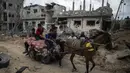 Warga Palestina menaiki kereta kuda yang penuh dengan barang-barang, melewati rumah-rumah yang hancur, di kota Beit Hanoun, Jalur Gaza utara, Jumat (21/5/2021).  Israel dan Hamas telah sepakat untuk gencatan senjata setelah 11 hari pertempuran. (AP Photo/ Khalil Hamra)