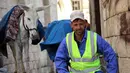 Seorang pekerja kota beristirahat di dekat keledai saat tugas hariannya mengumpulkan sampah rumah tangga di kota Akre, sekitar 500 km sebelah utara Baghdad, Irak, 13 Februari 2021. Pemerintah kota Akre menggunakan keledai dan anak kuda untuk mengumpulkan sampah. (SAFIN HAMED/AFP)