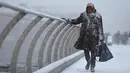 Seorang wanita melintasi jembatan milenium saat hujan salju turun di London (27/2). Cuaca ekstrem yang melanda sebagian wilayah Eropa menyebabkan warga dan wisatawan mengalami sakit dan beberapa meninggal akibat kedinginan. (AFP Photo/Daniel Leal-Olivas)