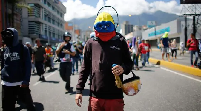Seorang pengunjuk rasa memakai topeng berwarna bendera Venezuela, saat ikut serta dalam demonstrasi anti-pemerintah ke Mahkamah Agung di Caracas, Venezuela, Kamis, 6 Juli 2017. (AP Photo / Ariana Cubillos)