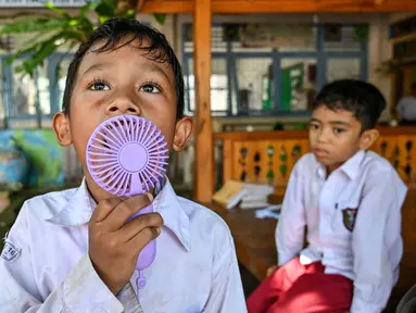 Seorang siswa menggunakan kipas angin portabel saat belajar di luar kelas selama gelombang panas di sebuah sekolah dasar di Banda Aceh pada 7 Mei 2024. (CHAIDEER MAHYUDDIN/AFP)